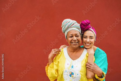 Happy african mother and her daughter wearing ethnic afro clothes while smiling in front of camera - Mom day, family and love concept