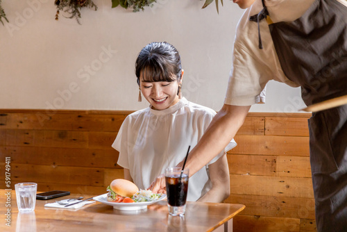 ランチを食べにカフェ・飲食店に来たアジア人女性と料理を運ぶ配膳する男性店員・スタッフ 