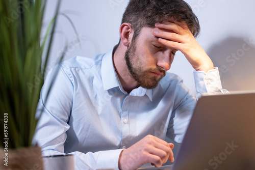 portrait d'un étudiant ou d'un employé de bureau fatigué et surmené assis devant son ordinateur portable. Il se tient la tête dans les mains.