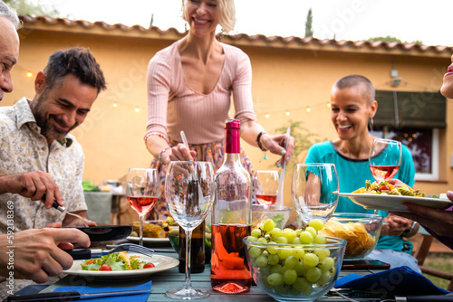 Caucasian woman serving salad to friends during outdoor garden dinner party. Friends having fun. Focus on foreground.