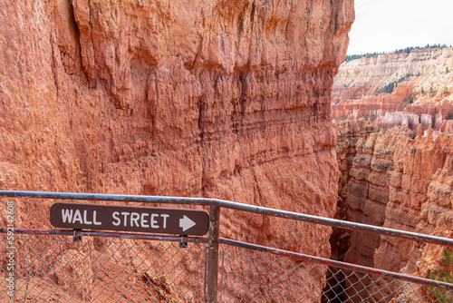 Wooden sign saying Wall Street on Navajo hiking trail in Bryce Canyon National Park, Utah, USA. Selective focus on informational sign. Barren desert landscape with view of natural amphitheatre
