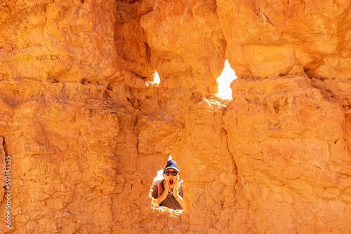 Woman making a peek a boo face through pinnacle rock looking like a face on Peekaboo hiking trail, Bryce Canyon National Park, Utah, USA. Hoodoo sandstone rock formations in natural amphitheatre