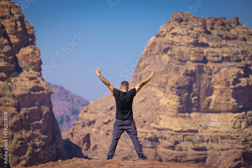 Petra w Jordanii. Mężczyzna stojący na szczycie skalnej góry na tle błękitnego, niebieskiego nieba. 