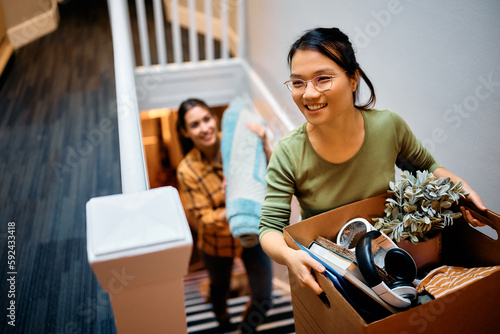 Happy Asian woman and her friend walking upstairs through hallway while moving in new apartment.