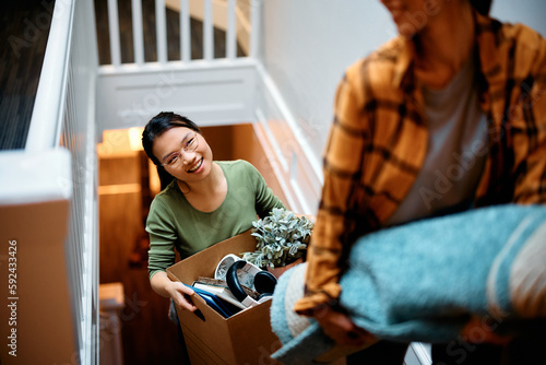 Happy Asian woman and her friend carrying their belongings upstairs while relocating into new apartment.