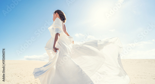 Calm woman in fashionable, maxi white wedding dress posing on the desert, dancing in sunny light