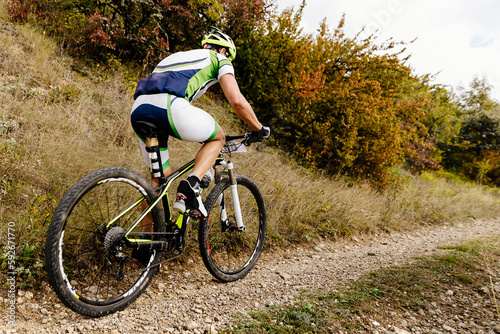 male cyclist riding mountain bicycle on gravel road with bushes on side in cross-country cycling competition