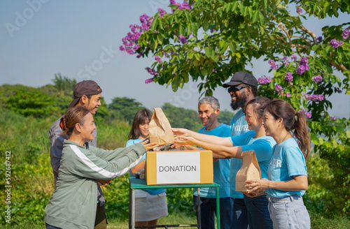 volunteers giving paper bag of food to asian senior woman and son,group of volunteers helping the needy to distribute of food items and water in the rural park