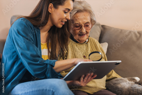 Nurse helping a senior lady to read news on a tablet, using magnifying glass.