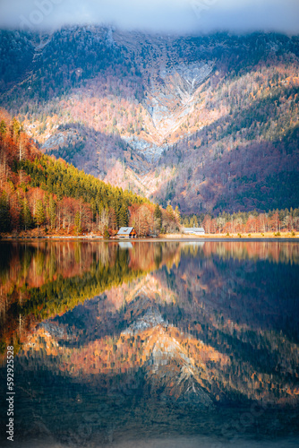 Vertical shot of a lake reflecting the colors of autumn trees and a high mountain covered in fog