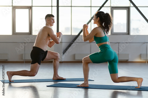 Smiling attractive man and woman doing health exercises indoors in fitness hall