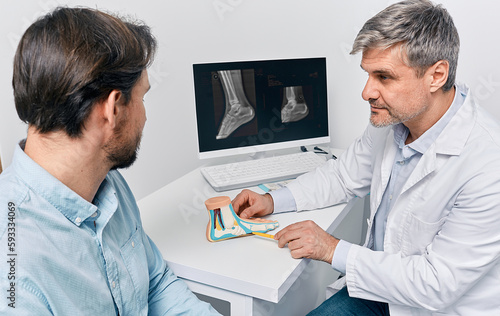 Orthopedic doctor consulting adult man with pes planus, explaining treatment methods using anatomical flat feet model. Treatment of flatfoot