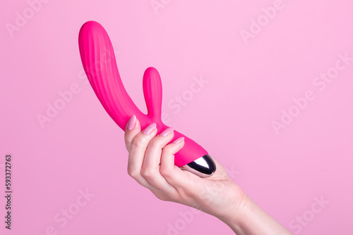 Pink sex toy rabbit shaped vibrator for women in female hand isolated on light pink background