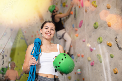 young positive muscular woman with necessary equipment stands in gym near climbing wall.Active leisure concept