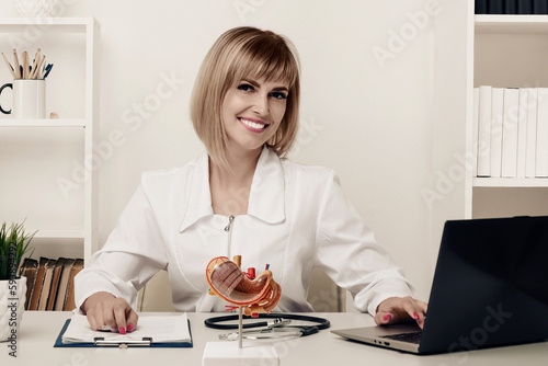 Young beautiful doctor woman working happy and smile in hospital, sitting on table, mockup stomach on work desk