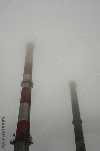 Smog w mieście, wysokie kominy przemysłowe w gęstej mgle. 