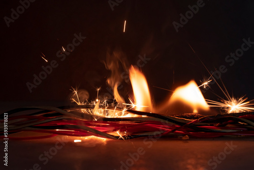 Electrical wiring and wires are lit on a dark background. A short circuit in the twisted wires from the computer. Flames, sparks and smoke