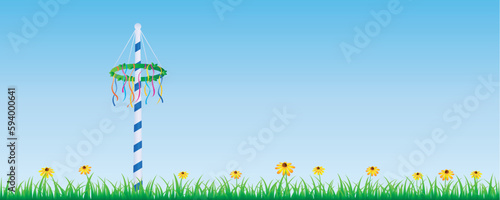 maypole with colorful ribbons on green meadow with flowers