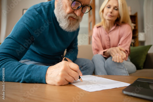 Senior Couple Filling In Form Signing Papers Sitting Indoors