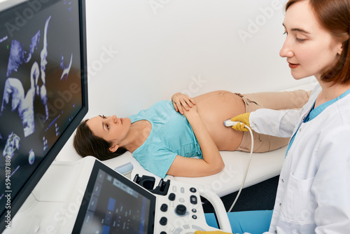 Prenatal testing. Ultrasound specialist doing third trimester screening of pregnant woman with ultrasound machine in medical clinic