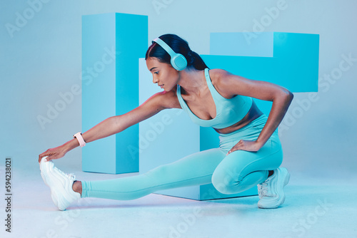 Headphones, stretching and fitness woman isolated on blue background for workout, training or exercise music. Legs, sports and biracial person listening to audio, muscle health and wellness in studio