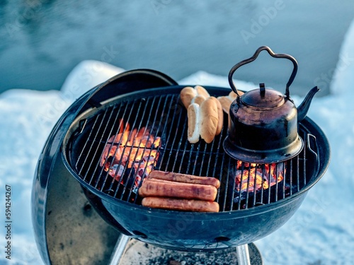 Grill grid with sausages, bread and tea pot on the lakeside in winter