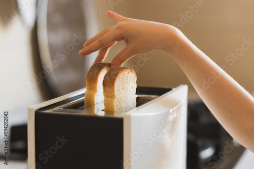 Close-up of a child's hand that inserts white slices of bread into a toaster.