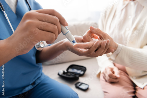 cropped view of multiracial nurse taking blood sample of senior woman with lancet pen.