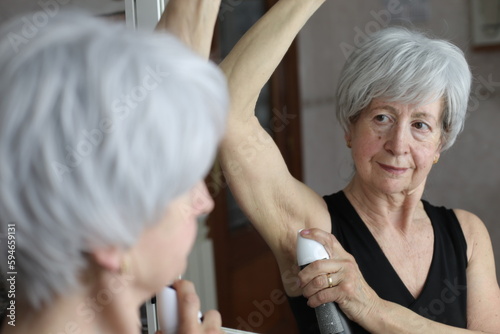 Senior woman applying deodorant in the bathroom 