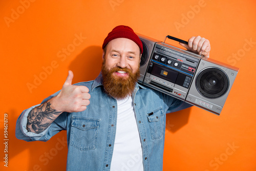 Photo of irish funny redhair guy thumb up dj music lover hold boom box retro party bearded tattooed person isolated on orange color background