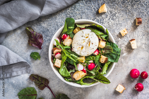 Mixed salad with radishes, homemade croutons and burrata cheese on gray background, top view