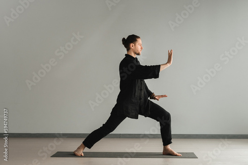 A man in black kimano practicing qigong energy exercises indoors