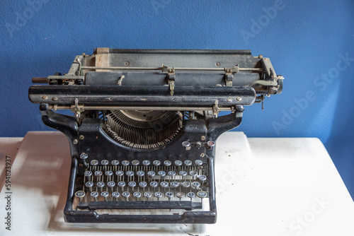 Antique Black Manual Typewriter on a White Desk Against a Blue Wall