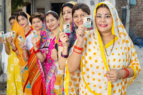 Group of happy traditional indian women standing in queue showing voter card id to cast vote at polling station. Election in india.