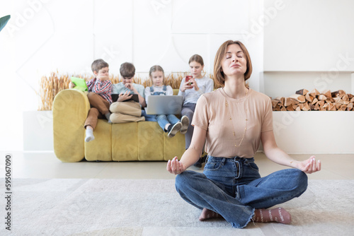 Young mother meditating on the floor while her children playing on background 