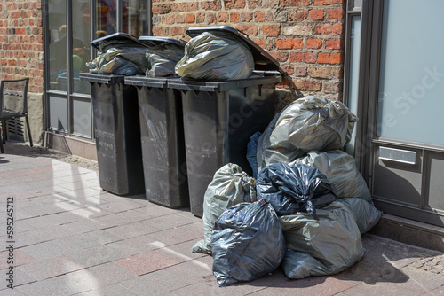 Overfilled trash bins and rubbish bags full of garbage on the pavement in the city, daily waste output from the affluent society