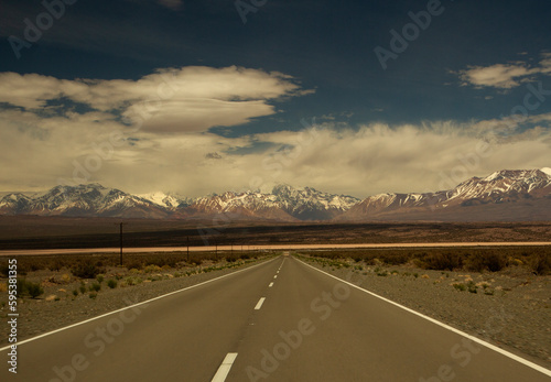 Traveling along the asphalt highway across the arid desert and into the Andes cordillera, under a beautiful blue sky with clouds.