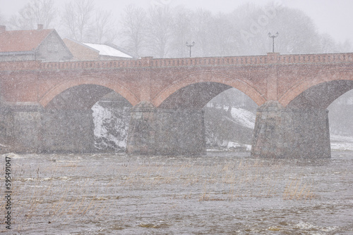 An old bridge from 1874 in Latvia made from bricks across a river on a cold and snowy Spring day
