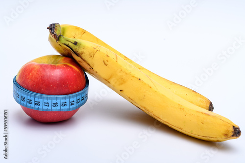 Dojrzały żółty banan oparty o czerwone jablko owinięte taśma mierniczą, centymetr krawiecki białe tło 