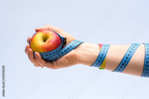 Jabłko trzymane w dłoni na jasnym tle owinięte centymetrem krawieckim do mierzenia obwodów 