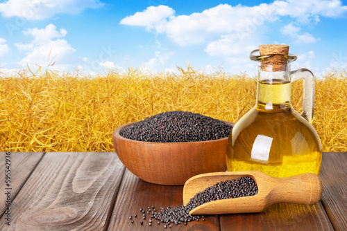 rapeseed oil in bottle with dry rape seeds in bowl on table and agriculture field as background