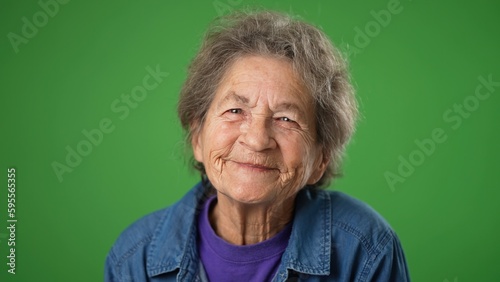 Closeup funny portrait of happy smiling toothless elderly senior old woman with wrinkled skin and grey hair on green screen background.