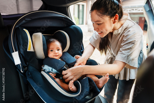 happy mother is fastening safety belt to newborn baby in car seat