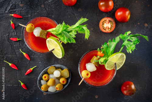 Bloody Mary cocktail with garnish on a black background, overhead flat lay shot. Spicy tomato juice with alcohol, lime, pickles, celery, and peppers