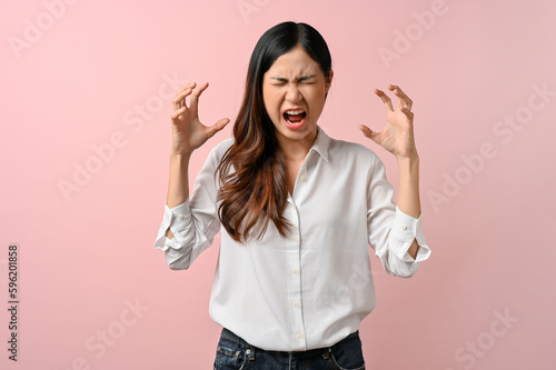 Upset Asian woman having a headache on pink isolated background.