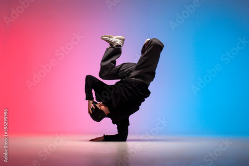 guy hiphop performer break dance in neon club lighting and doing acrobatic trick, male dancer stands in acrobatic pose