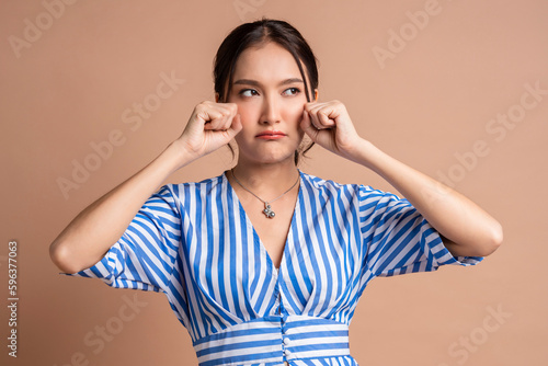 asia woman hand gesture pretend crying fashion photo shoot,sadness asian female woman look at camera hand clean tear drop from her eye studio shot on brown colour background