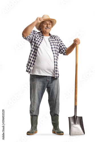 Full length portrait of a happy mature farmer with a shovel greeting with hat