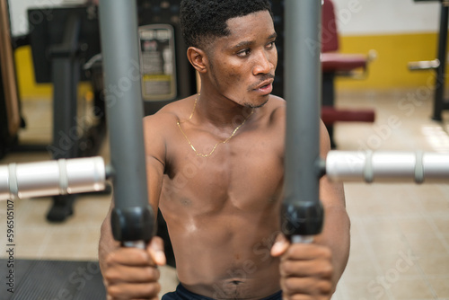 A young African male in a gym, exercising for physical fitness and well-being with weight training to build their muscular strength.