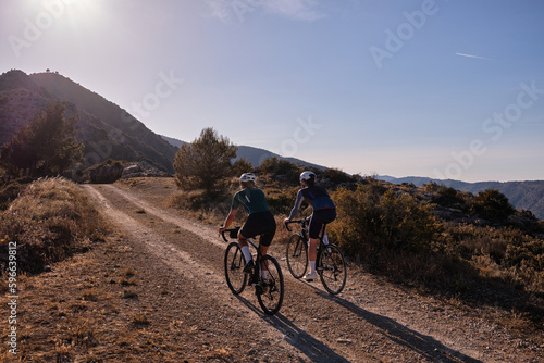 Gravel adventure..Back view of professional gravel cyclists riding uphill with mountain view at sunset. Alicante region in Spain 